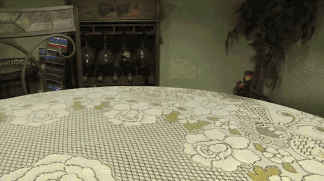 a round table with a lace table cloth and a wine rack in the background