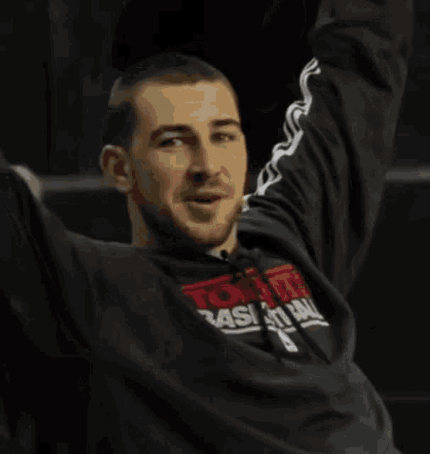 a man wearing a toronto basketball shirt is sitting with his arms outstretched and says victory baby !