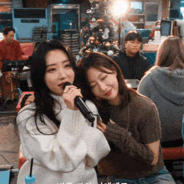 a woman singing into a microphone while another woman looks on
