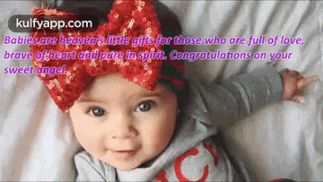 a baby with a red bow on her head is laying on a bed with a congratulations message .