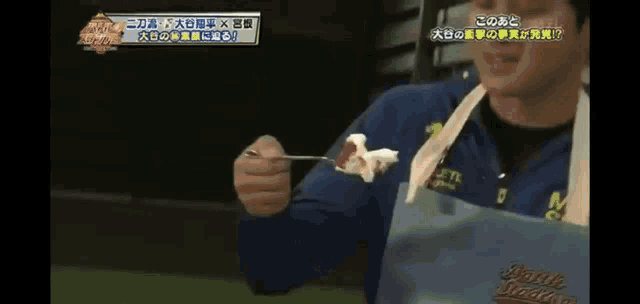 a man wearing an apron is holding a spoon with a piece of food on it .