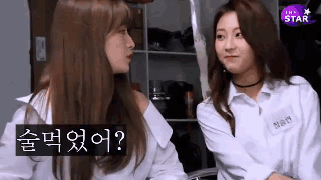 two girls are sitting next to each other in a room and talking to each other in korean .