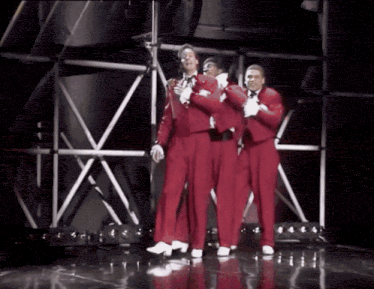 three men in red tuxedos and white gloves are dancing on a stage