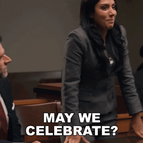 a woman in a suit says may we celebrate in front of a group of people