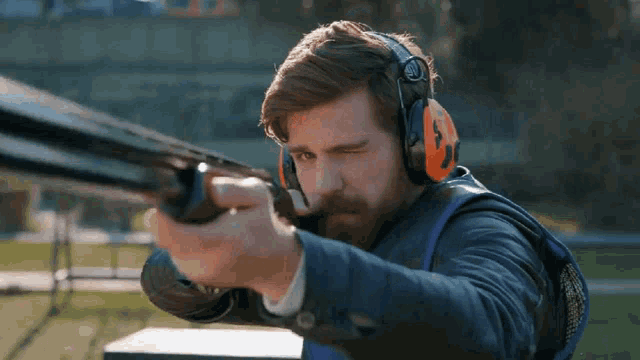 a man wearing ear protectors is aiming a shotgun