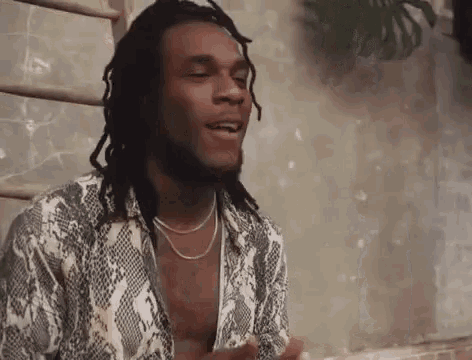 a man with dreadlocks and a snake print shirt is sitting on a ladder .