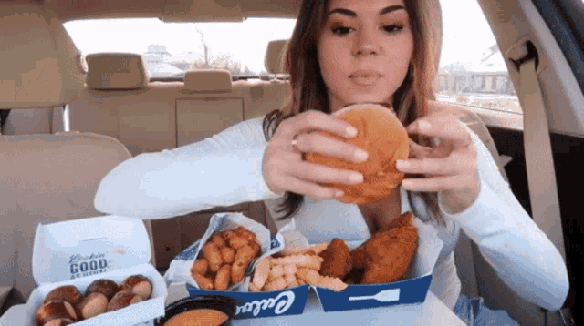 a woman in a car is eating a hamburger and pretzels from a box that says ' chicken ' on it