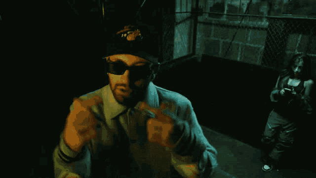 a man wearing sunglasses and a hat that says ' a ' on it stands in a dark room