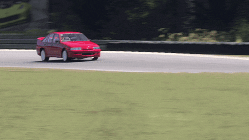 a red car is driving on a track with a fence in the background