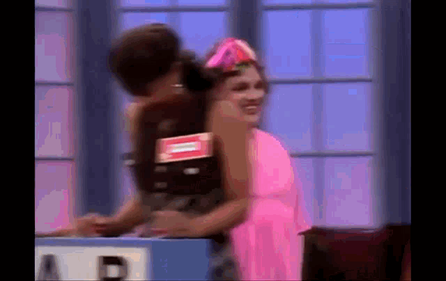 a man in a pink dress is hugging a woman in a pink dress on a game show .