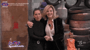 two women standing next to each other in front of tires and a sign that says #grandefratello
