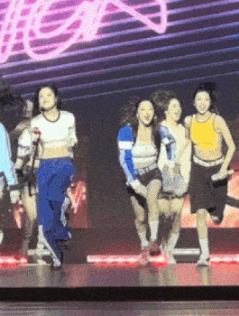 a group of young women are dancing on a stage in front of a neon sign that says ' a ' on it