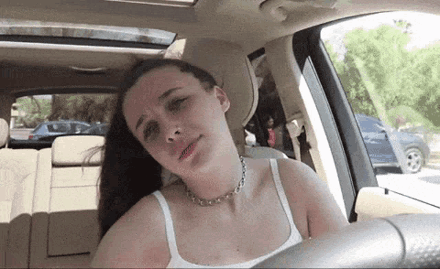 a woman in a white tank top is sitting in a car