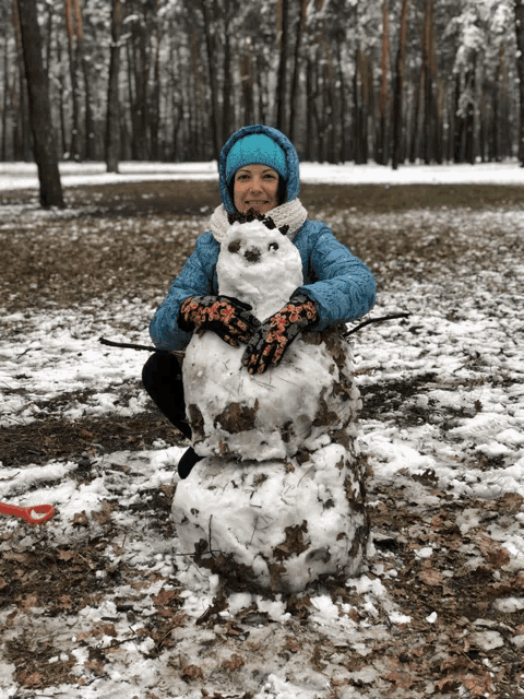 a woman in a blue jacket is holding a snowman