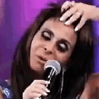 a woman is singing into a microphone while another woman scratches her forehead .
