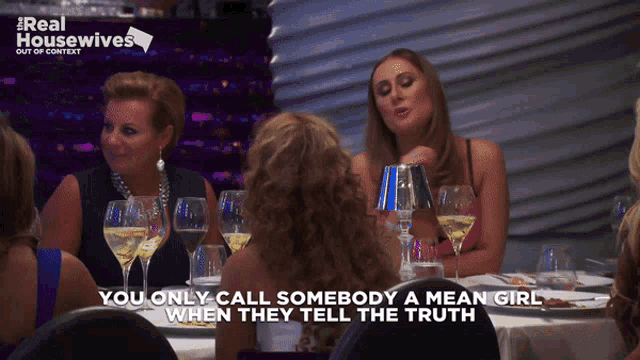 a group of women sitting at a table with a real housewives logo on the bottom