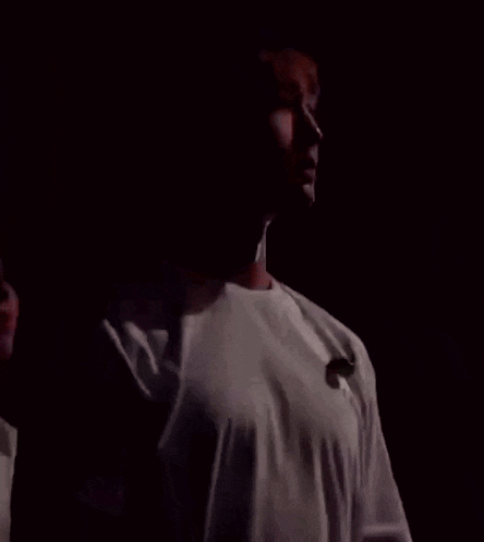 a man in a white shirt is standing in a dark room with his eyes closed .