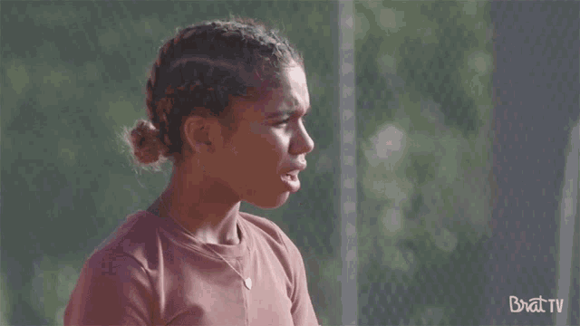 a girl stands in front of a fence with the words brat tv on the bottom right