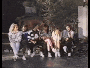 a group of people are sitting on a bench and talking to each other .