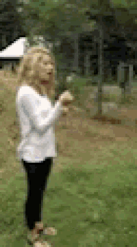 a woman in a white shirt and black pants is standing in a field .