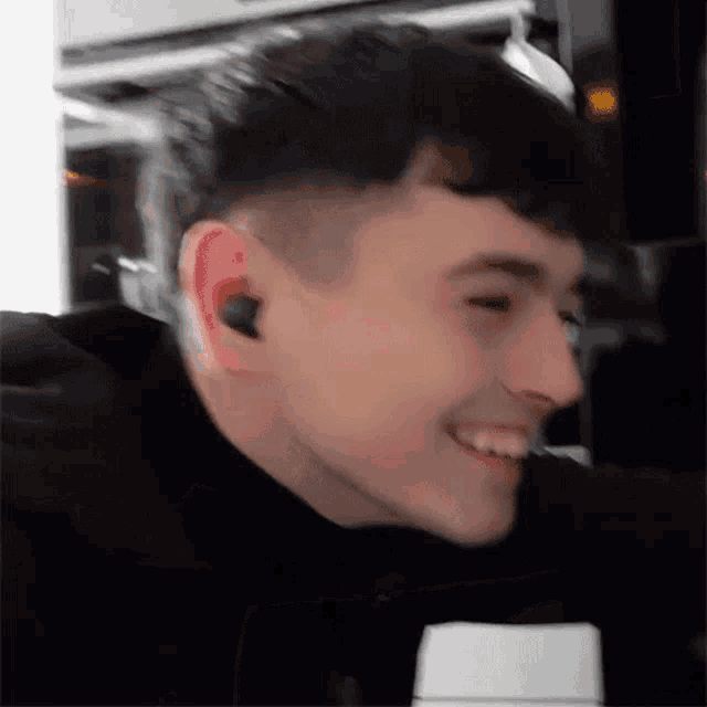 a young man wearing ear buds is smiling in a blurry photo