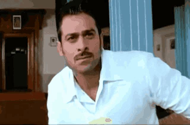 a man with a mustache and a white shirt is standing in a room