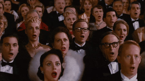 a crowd of people in tuxedos and glasses singing with their mouths open