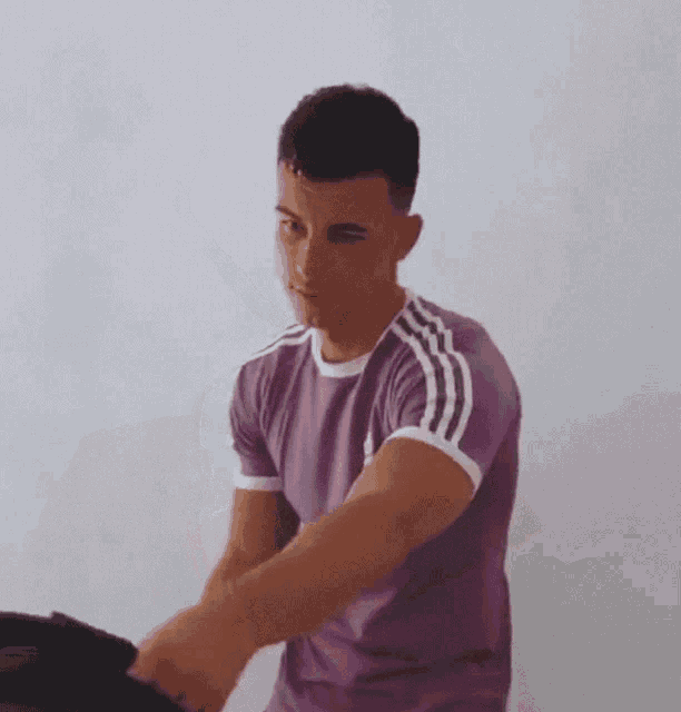 a man in a purple adidas shirt is holding a black bag and making a funny face .