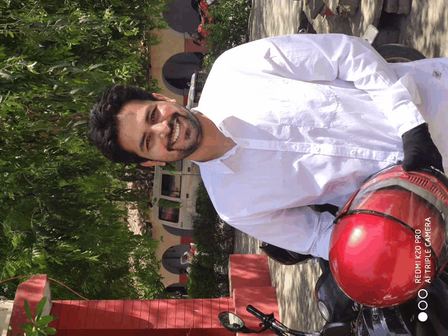 a man in a white shirt is standing next to a red motorcycle with a red helmet