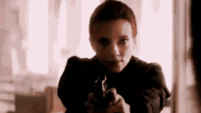 black widow is holding a gun in her hand and pointing it at a person .