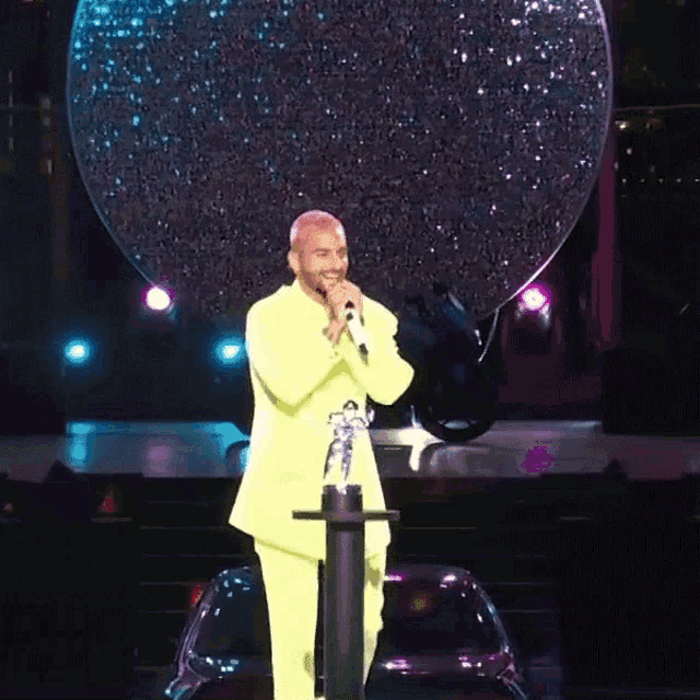 a man in a yellow suit sings into a microphone on a stage