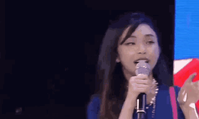 a woman in a blue shirt is holding a microphone in front of a blue screen .