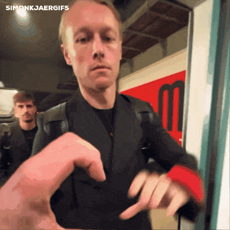 a man in a black jacket is standing in front of a red sign that says simonkjaergifs