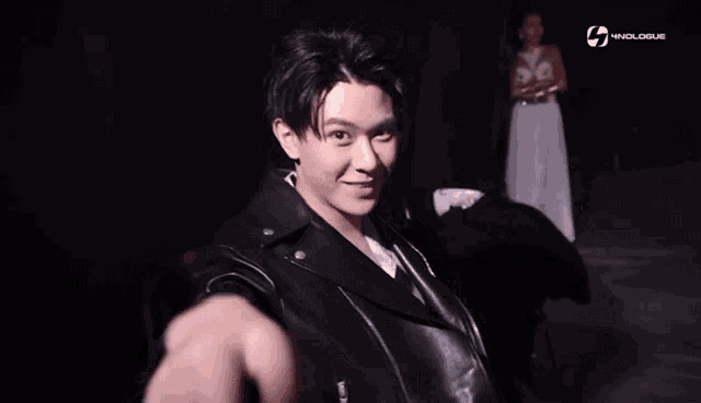 a man wearing a black leather jacket is smiling in front of a woman in a white dress