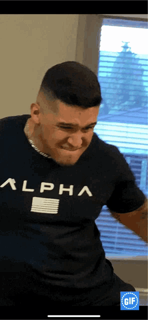 a man wearing a black alpha t-shirt is making a funny face