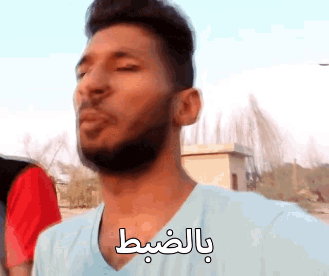 a man with a beard is wearing a blue shirt with arabic writing