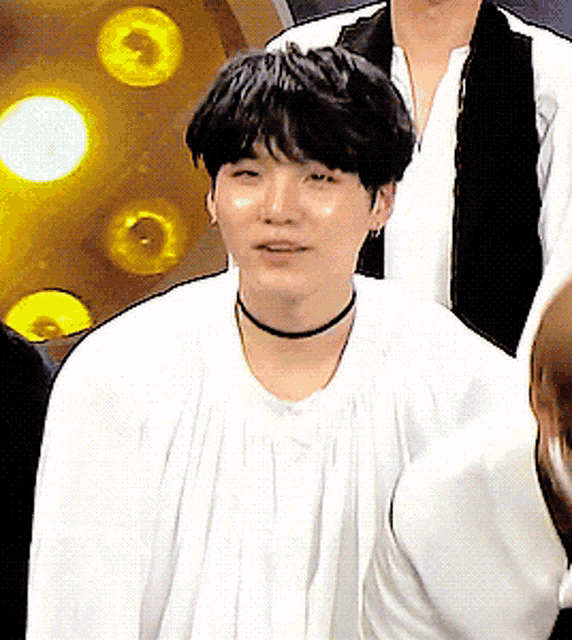 a young man wearing a white shirt and a black choker looks at the camera