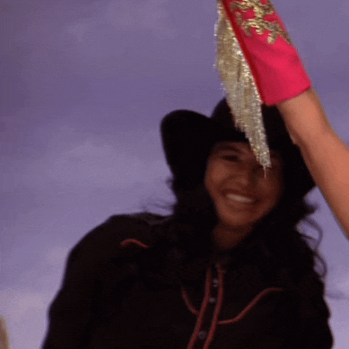 a woman wearing a cowboy hat and a pink glove with gold fringe is smiling