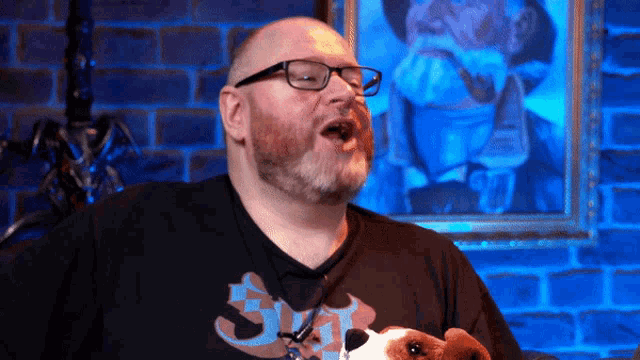 a man wearing glasses holds a stuffed animal in front of a painting