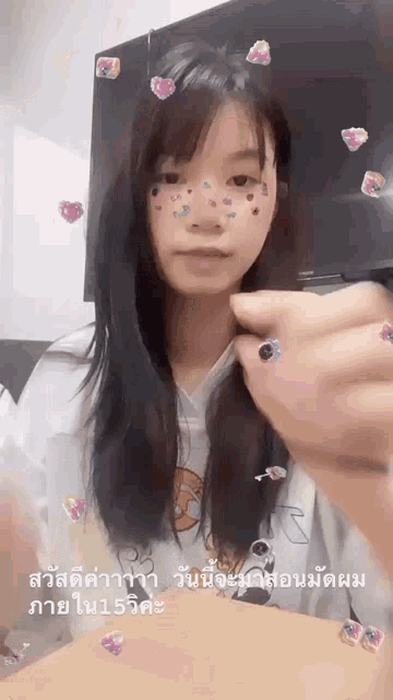 a girl with long hair and hearts on her face is sitting at a table with her hands in her hair .