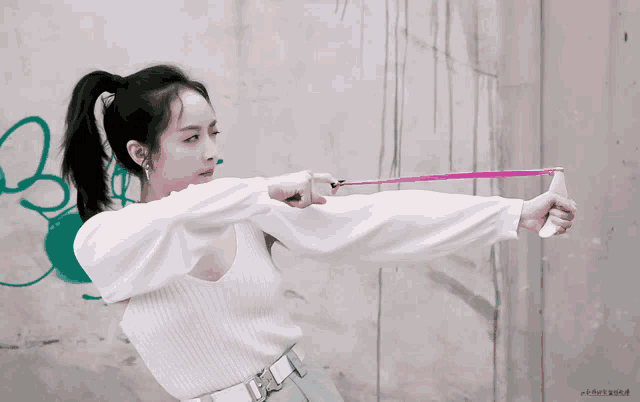 a woman in a ponytail is holding a pink object in front of a wall that has the letter b on it