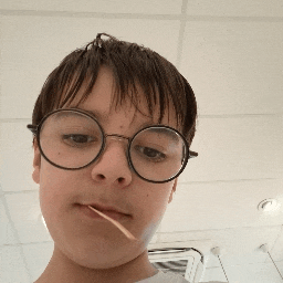 a young boy wearing round glasses has a toothpick in his mouth