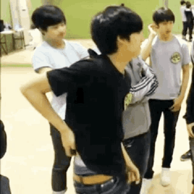 a group of young men are standing in a room . one of the men is wearing a black shirt .