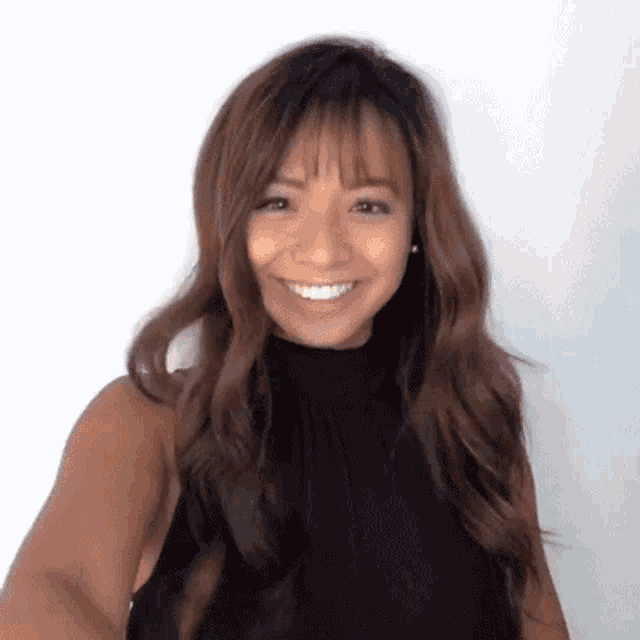 a woman with long brown hair and bangs is smiling and wearing a black top .