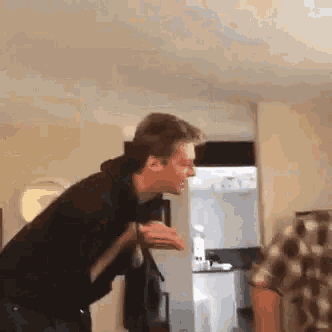 a man in a black hoodie is standing in a living room with his hands outstretched .