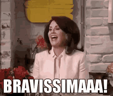 a woman in a pink suit is laughing with the words bravissimaa written on the screen .
