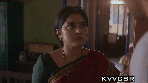 a woman in a red and green saree is looking at a man .