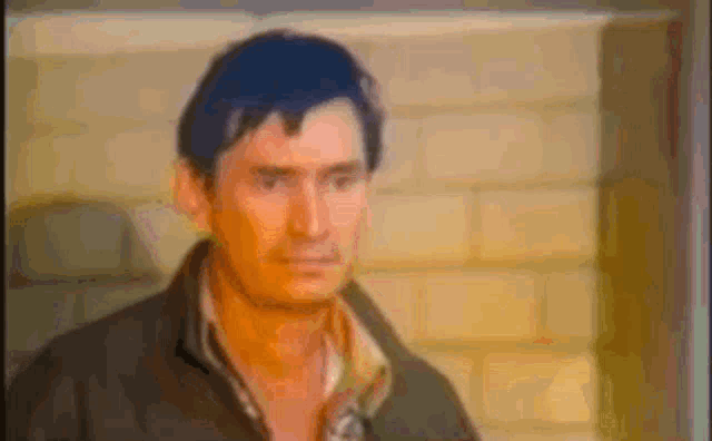 a man with blue hair is standing in front of a brick wall and looking at the camera .
