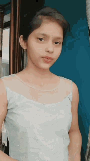 a young girl wearing a white top is standing in front of a blue curtain