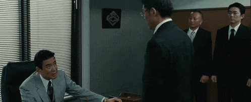 a man in a suit and tie is talking to another man in a room